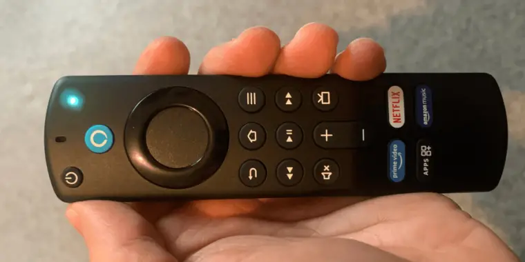 Fire TV remote with a blue light glowing at the top, held in a person's hand, likely indicating that the device is active or listening.