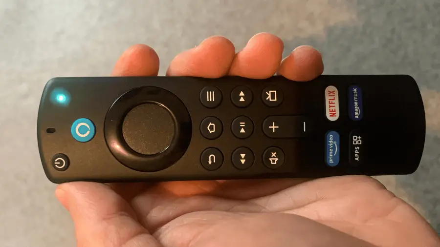 Fire TV remote with a blue light glowing at the top, held in a person's hand, likely indicating that the device is active or listening.