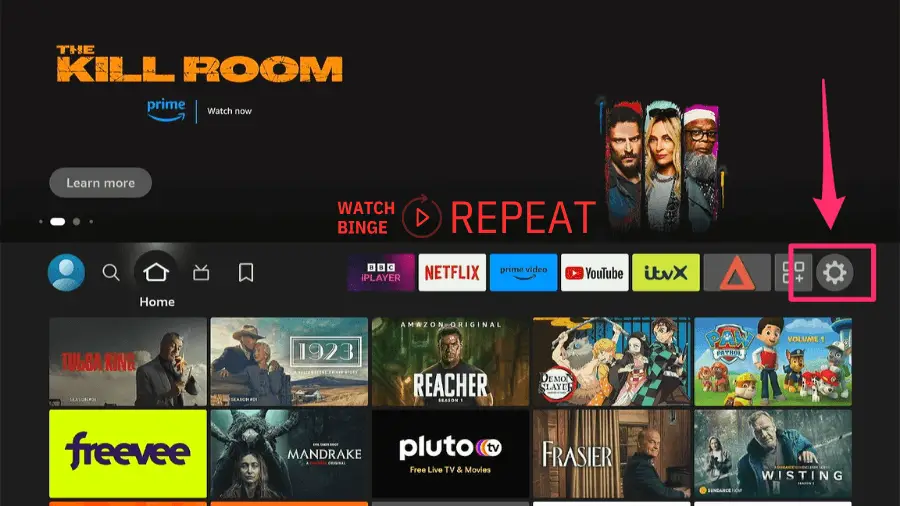 Amazon Firestick homepage on a TV screen with various streaming service icons and a settings gear highlighted by a red arrow.