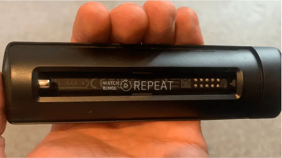 battery compartment of a Firestick remote control held in hand, with batteries ejected and a label inside with text and symbols, suggesting proper battery orientation.