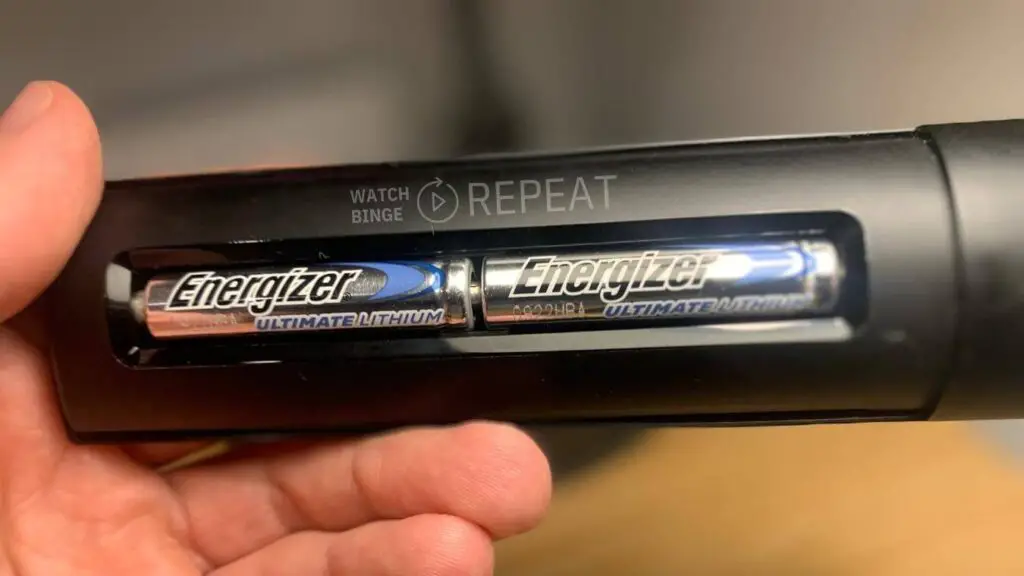 Two Energizer Ultimate Lithium batteries are inserted in the back of a Firestick remote, held by a hand."