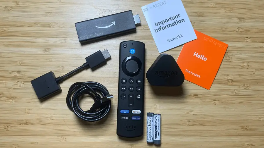 A collection of Amazon Fire TV Stick components and documentation laid out on a wooden surface, including a remote control, the Fire TV Stick itself, a power cable, an HDMI extender, batteries, and informational booklets.