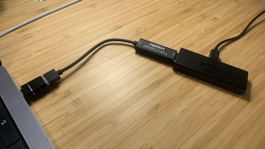 A USB-C to USB-A adapter and an HDMI to USB-C video capture card are laid out on a wooden surface, connected by a USB cable and Firestick.

