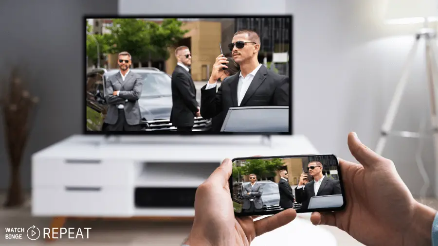 A person holding a smartphone mirroring a security agent on the phone screen, with the same image on a TV in the background.